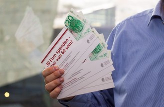 Eine Hand hält fächerartig angeordnete Flyer zur Aktion "30 Euro spenden - einer von 60 sein". Bild: Paul Glogowski