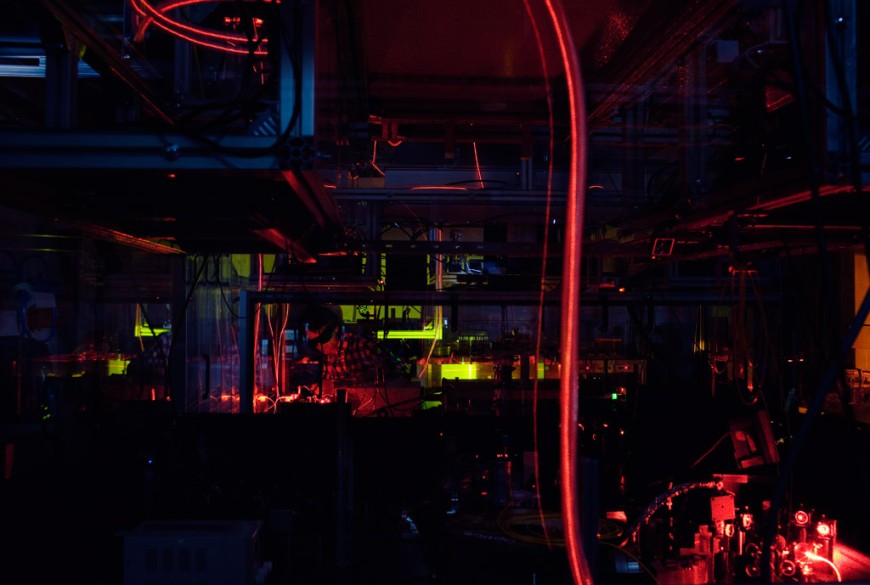 Blick über den Laser-Aufbau zum Lichtspeicher-Experiment. Im Bild sind Lichtleitfasern zu sehen, die die orange Laserstrahlung an das Experiment (im Hintergrund) führen. Bild: Katrin Binner