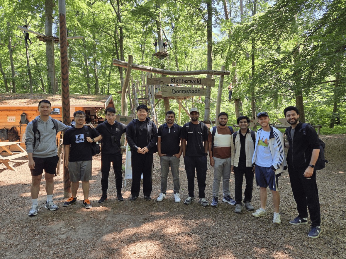 Masterstudierende der TU Darmstadt genießen einen Tag voller Abenteuer in einem Hochseilgarten. Dieses Bild zeigt die Gruppe während einer der sozialen Veranstaltungen des MasterPlus-Programms. Die Teilnehmenden posieren in einer malerischen Waldlandschaft, umgeben von grünen Blättern und Bäumen. 