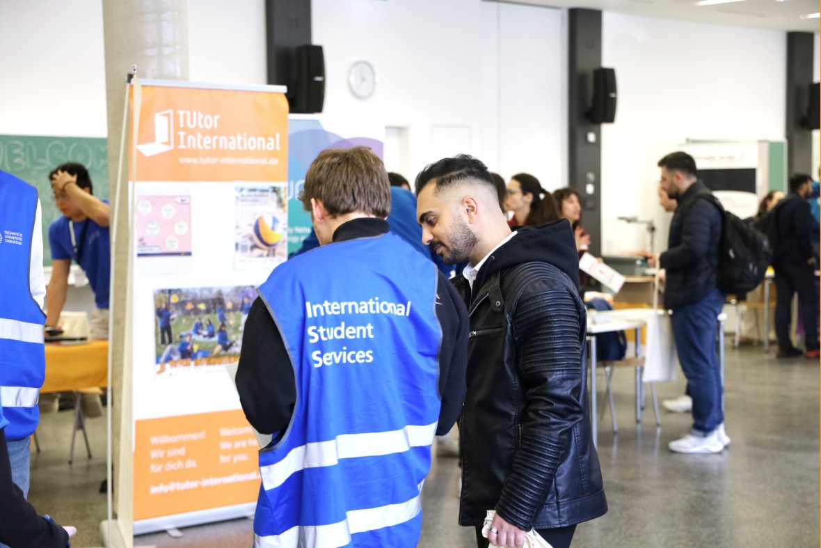 A MasterPlus Buddy in a blue vest is explaining something to a student. MasterPlus Buddies support new Master's students at TU Darmstadt.