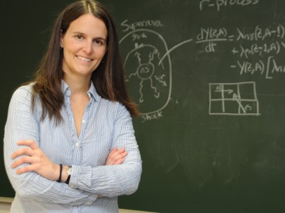 Die Physikerin Almudena Arcones schaut vor einer Schultafel lächelnd in die Kamera. Bild: Otto Gabriele / GSI