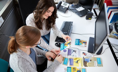 Franziska Ritter (ZSB) and student ambassador Denise at a desk looking at a veriety of flyers and brochures together.