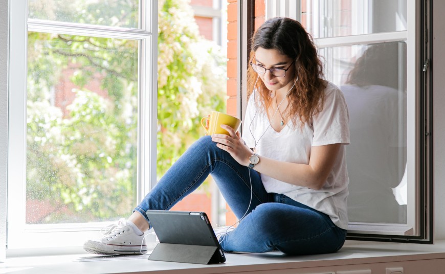 Studentin sitzt mit Tablet vor einem Fenster