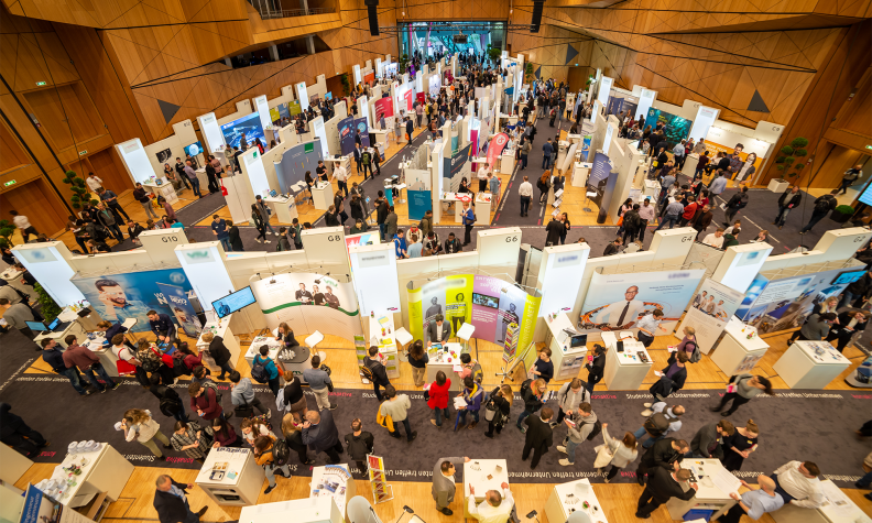 #studentsofTUdarmstadt, Berufseinstieg: konaktiva Unternehmenskontaktmesse, Blick von oben auf Messestände und Messebesucher:innen. // #studentsofTUdarmstadt, career entry: konaktiva company contact fair, view from above of fair stands and fair visitors.