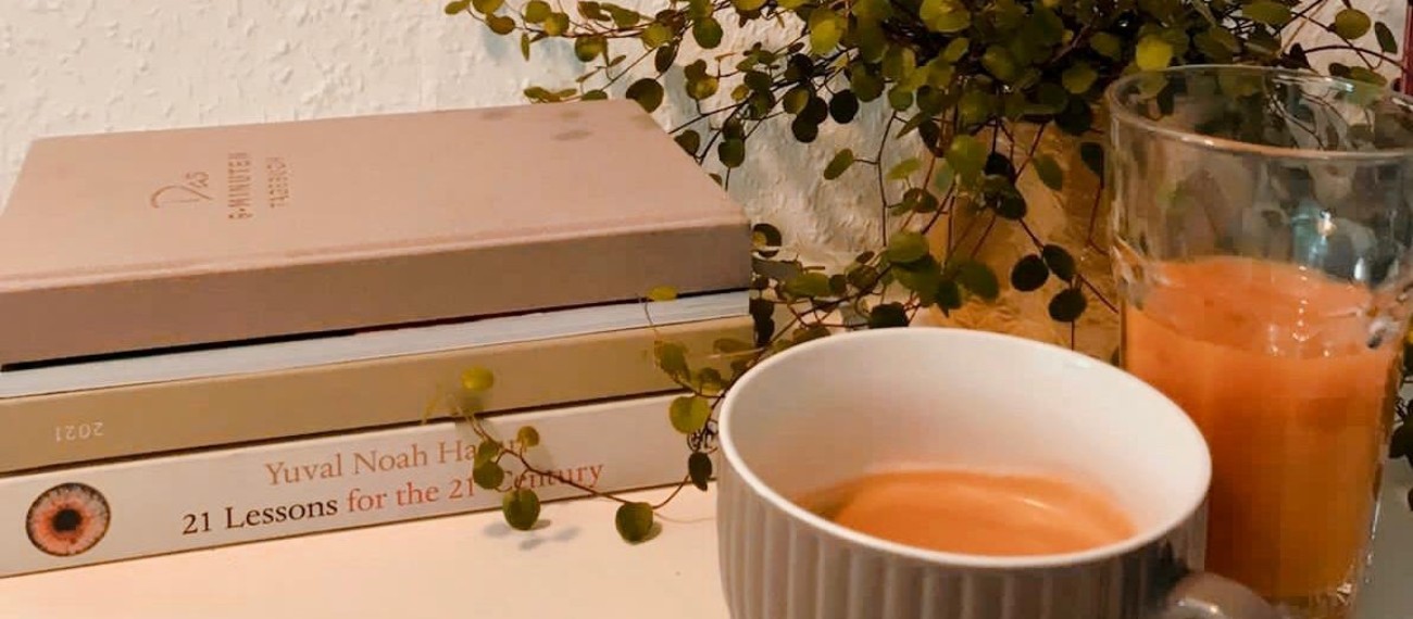 Bücherstapel neben Zimmerpflanze. Tasse Kaffee und ein Glas mit Saft im Vordergrund.