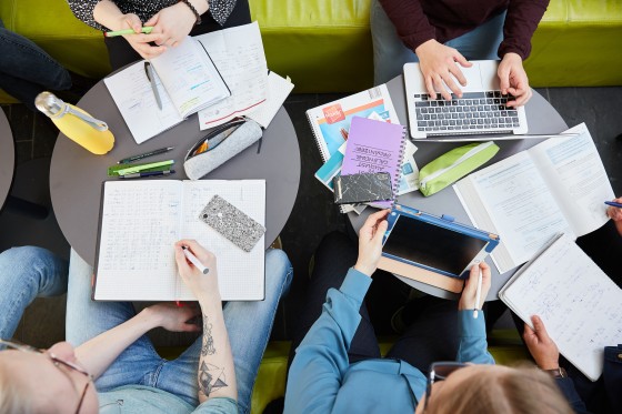 Blick von oben auf vier Studierende und auf ihre Lernutensilien.
