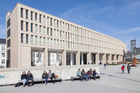 Foto der Universitäts- und Landesbibliothek Darmstadt (ULB) an einem sonnigen Tag. Im Vordergrund sind Studierende auf Bänken.